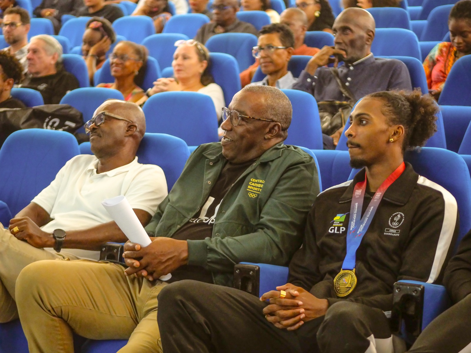 Des personnes réunies dans un auditorium ; au premier plan, l’une porte une médaille.